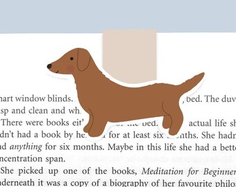 Peut inclure: Un marque-page en forme de dachshund brun avec un contour blanc. Le marque-page est sur une page d'un livre avec du texte sur la méditation et une biographie.