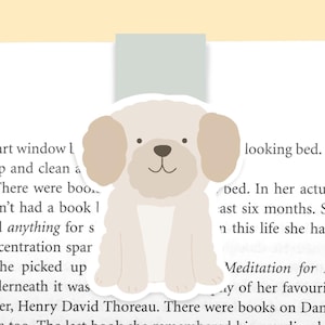 May include: A beige dog bookmark with a light blue background. The dog is sitting with its paws together and has a happy expression. The bookmark is designed to hold a page in a book.