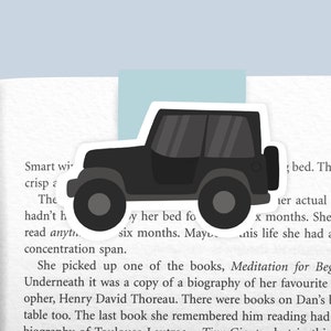 May include: A black Jeep bookmark with a white outline. The bookmark is partially covering a page of a book with text about reading.