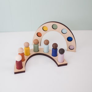 Op de afbeelding: Houten regenboog speelgoed met kleurrijke houten poppetjes. De regenboog boog heeft 8 plekken voor de poppetjes om in te staan. De poppetjes zijn in verschillende kleuren geverfd.
