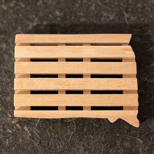 May include: A wooden soap dish shaped like the state of South Dakota. The dish has a slatted design to allow for drainage.