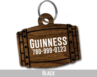 Puede incluir: Una chapa para perro de madera con forma de barril con el texto "GUINNESS 780-999-0123" en letras blancas. La chapa es negra con un llavero plateado.