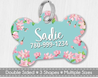 May include: A light blue bone-shaped dog tag with a pink floral pattern. The tag has the name "Sadie" and the phone number "780-999-1234" printed in white.