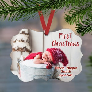 May include: A white metal ornament with a photo of a baby sleeping in a bucket. The ornament is decorated with the text "First Christmas", "Olivia Harper Smith", and "09.16.2018".