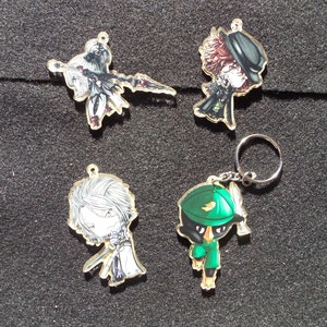 May include: Four colorful character keychains with gold accents. The keychains feature a black and white character with a sword, a black and red character with a hat, a white character with a sword, and a green character with a hat.