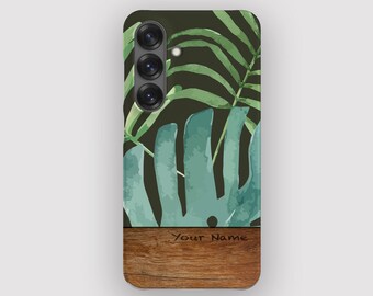 May include: A phone case featuring a watercolor design of green tropical leaves against a dark background. The bottom section has a wood grain texture with the text "Your Name". The case has a camera module.