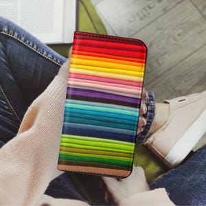 Pode incluir: Uma capa de telefone colorida com um padr&atilde;o de listras arco-&iacute;ris. A capa &eacute; de couro e tem uma borda marrom.