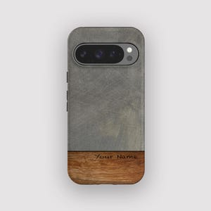 Może przedstawiać: Etui na telefon z szarą, teksturowaną górną częścią i dolną częścią z brązowego drewna. Etui na telefon ma wycięcie na aparat, a na drewnie wygrawerowano napis "Your Name".