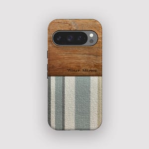 May include: A phone case with a wood grain top and a striped fabric bottom. The wood grain section has a camera cutout and the text "Your Name" engraved. The fabric features vertical stripes in shades of blue, white, and tan.