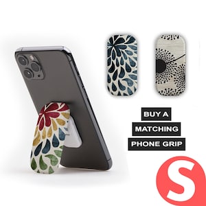 Pode incluir: Um smartphone preto com um agarre de telefone preso na parte de tr&aacute;s. O agarre do telefone &eacute; um design floral colorido com cores vermelho, amarelo, verde e azul. O telefone est&aacute; em p&eacute; sobre uma superf&iacute;cie branca. A imagem tamb&eacute;m mostra outros dois agarres de telefone com designs diferentes. O texto "BUY A MATCHING PHONE GRIP" est&aacute; escrito em letras brancas sobre um fundo preto. A letra "S" est&aacute; escrita em letras brancas sobre um c&iacute;rculo vermelho.