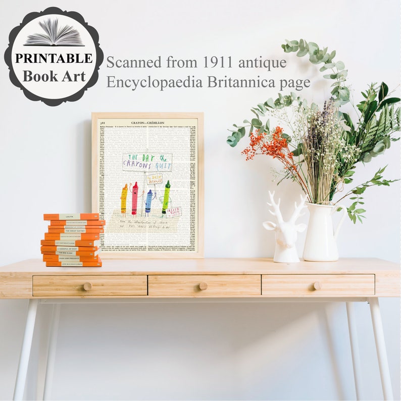 May include: A framed print featuring a vintage page from the 1911 Encyclopaedia Britannica, with a colorful crayon illustration and the text "THE DAY the CRAYONS QUIT." A stack of orange books sits to the left. A white vase with flowers is on the right.