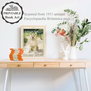 May include: A framed print of a book cover featuring a dog and the text "KATE DICAMILLO Because of Winn-Dixie". The print is on a wooden desk with a stack of books and a vase of flowers.