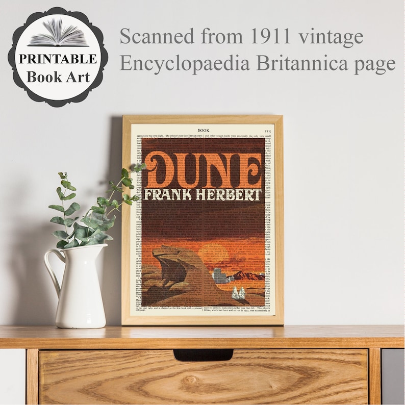 K&ouml;nnte beinhalten: Ein gerahmter Druck eines Buchcovers f&uuml;r "Dune" von Frank Herbert. Das Cover zeigt einen Sandwurm vor einem Sonnenuntergangshintergrund. Der Buchtitel ist in gro&szlig;en, fetten Buchstaben gedruckt und der Name des Autors ist darunter gedruckt. Der Druck ist in einem einfachen Holzrahmen gerahmt.