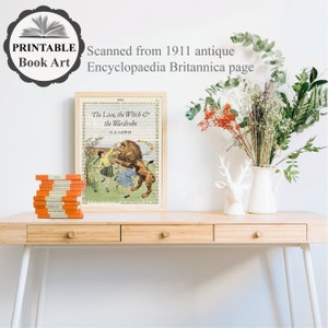 May include: A framed print of "The Lion, the Witch & the Wardrobe" on a vintage book page, with a stack of orange books. The print is on a light wood desk with a white vase of flowers and a deer head figurine. Text on the print reads "PRINTABLE Book Art" and "Scanned from 1911 antique Encyclopaedia Britannica page."