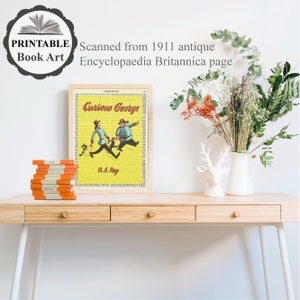 May include: A vintage book page print featuring a yellow background with the text "Curious George" and an illustration of two people and a monkey. The print is framed and displayed on a wooden table with a vase of flowers and a decorative deer statue.