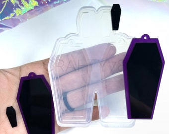 May include: A clear silicone mould with four coffin-shaped cavities. The mould is used to create resin earrings or charms. The mould is shown with purple resin pieces in the cavities.