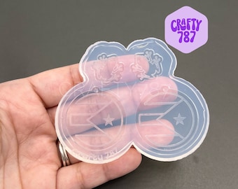 Könnte beinhalten: Transparente Silikonform mit zwei runden Abdrücken eines Sterns und diagonalen Linien, die an eine Flagge erinnern. Die Form ist mit "Crafty 787" beschriftet.
