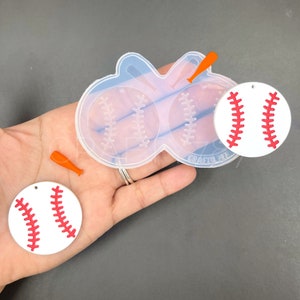 May include: A silicone mold for making baseball-themed earrings. The mold has two baseball shapes and two bat shapes. There are two finished baseball earrings in the image, one is white with red stitching and the other is white with red stitching.