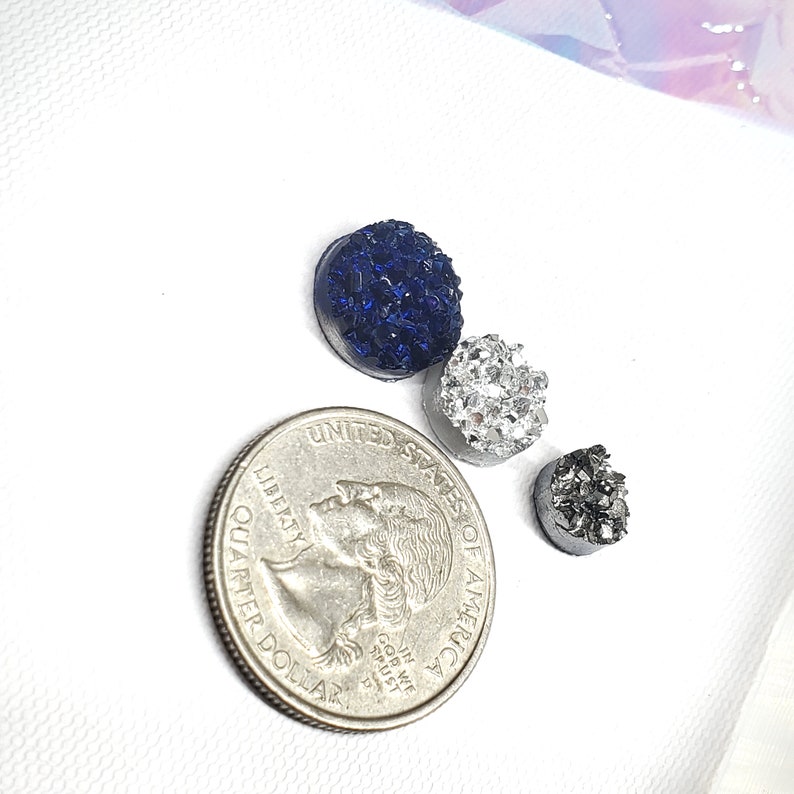 May include: Three druzy-style cabochons in navy blue, silver, and charcoal gray, next to a quarter. The cabochons have a textured, crystalline surface. The quarter is included for size reference.