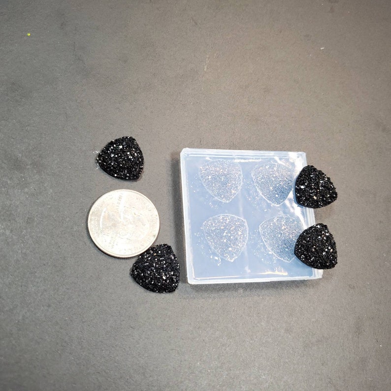 Pu&ograve; includere: Quattro cabochon in resina di forma triangolare nera con una finitura scintillante. I cabochon sono accanto a uno stampo in silicone trasparente con quattro cavit&agrave; di forma triangolare.