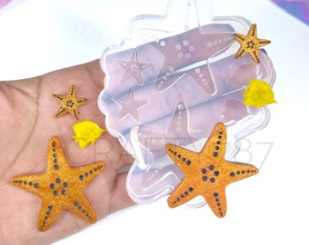 May include: A clear silicone mold with five starfish shapes. The mold is on a hand holding several orange starfish with black dots.
