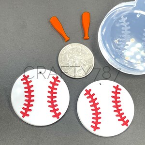 May include: Two white baseball-shaped resin earrings with red stitching. The earrings are shown next to a quarter and two orange baseball bats.