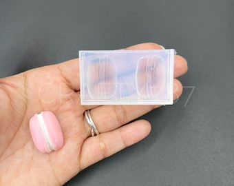 May include: A clear silicone mold with two cavities shaped like macarons. A pink macaron is shown next to the mold.