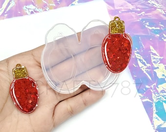 May include: Two clear silicone molds for making Christmas light ornaments. The molds are shaped like light bulbs and have a small hole at the top for hanging. Two red glitter Christmas light ornaments are shown next to the molds.