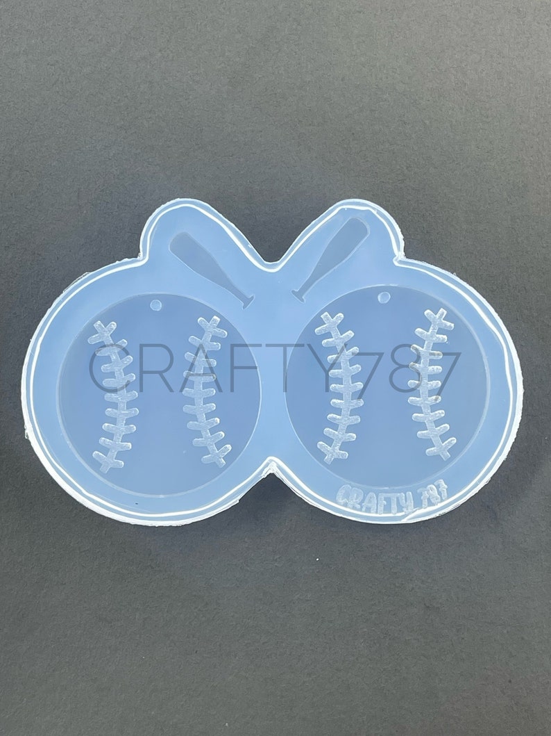 May include: Clear silicone mold with two baseball shapes and two bats. The mold is designed to create resin earrings or charms.