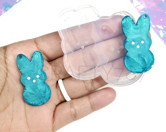 May include: Two teal blue bunny shaped resin molds with white dots. The molds are sitting on a hand with a clear silicone mold in the background.