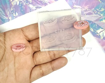 May include: A clear silicone mold with four donut shapes and the text "C787". A pink donut is next to the mold.
