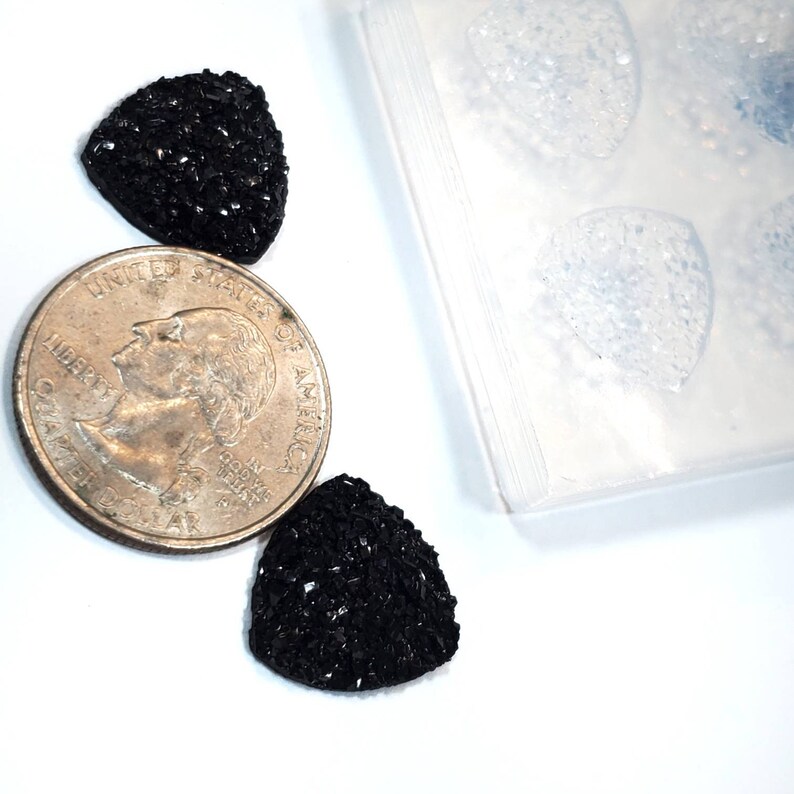 Pu&ograve; includere: Due strass neri a forma di triangolo con una superficie testurizzata, accanto a una moneta da un quarto di dollaro americano.