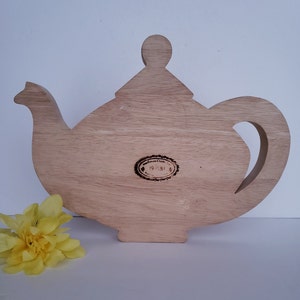 May include: Wooden teapot-shaped cutting board with a brown oval label that reads "Mackenzie Creek 1983".