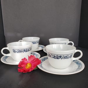 May include: Set of four white ceramic teacups with blue floral designs and matching saucers.