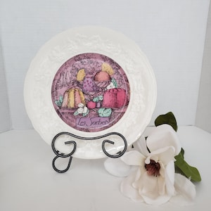 May include: A white ceramic plate with a raised embossed border and a central illustration of various sorbets and desserts. The image features pink and yellow tones with the text Les Sorbets printed in a script font at the bottom center.