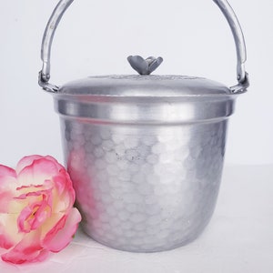 May include: Silver aluminum ice bucket with a hammered finish and a flower-shaped lid. The bucket has a handle and is perfect for keeping drinks cold.