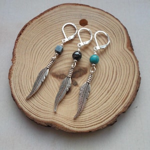 Puede incluir: Tres pendientes de plumas de plata con detalles de piedras preciosas. Los pendientes tienen un dije de pluma de plata, un aro de plata y una cuenta de piedra preciosa. Las piedras preciosas son negras, negras y turquesa.
