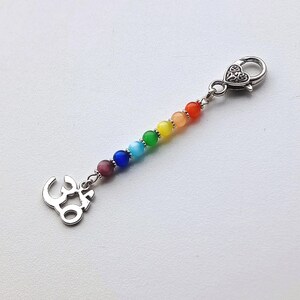 May include: A silver-toned charm with a rainbow of beads, including red, orange, yellow, green, blue, purple, and pink. The charm features a decorative clasp and an Om symbol pendant, perfect for a keychain or bag accessory.