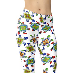 Op de afbeelding: Witte leggings met een kleurrijk patroon van gestileerde schildpadden. De schildpadden zijn versierd met felle kleuren, waaronder rood, blauw, groen, geel en oranje. De leggings zijn gemaakt van een rekbare, comfortabele stof.