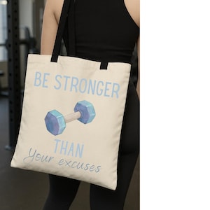 Könnte beinhalten: Cremefarbene Tragetasche mit schwarzen Trägern. Auf der Tasche steht in hellblau "BE STRONGER THAN Your excuses" und ein Aquarell-Hantel in Blau und Lila. Ideal für Fitness.
