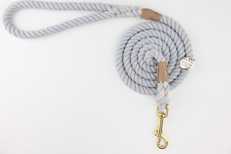 Pu&ograve; includere: Un guinzaglio per cani grigio chiaro realizzato in corda spessa e ritorta. Il guinzaglio &egrave; arrotolato e presenta inserti in tessuto beige e un moschettone e ferramenta in metallo color oro. L'impugnatura &egrave; ad anello per un facile trasporto.