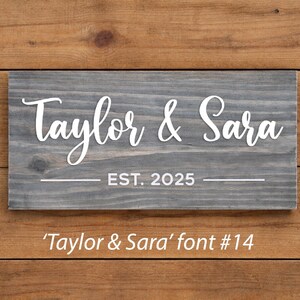 May include: A rectangular wooden sign with the names "Taylor & Sara" in white script, and "EST. 2025" below. The sign is gray and set against a wooden background. The text "'Taylor & Sara' font #14" is at the bottom.