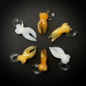 May include: Six glass tooth charms, some are white and some are yellow. The charms have a loop at the top for hanging.