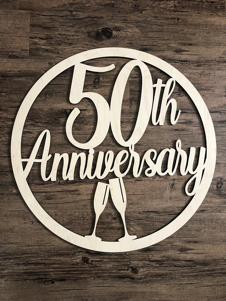 May include: A white wooden circle with the text "50th Anniversary" and two champagne glasses.