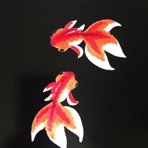 以下が含まれることがあります： 赤と白のディテールが施された、刺繍された金魚のアップリケが2つ。魚は異なる方向を向いています。