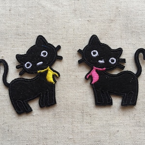May include: Two black felt cat appliques with embroidered details. One cat has a yellow bow and the other has a pink bow.