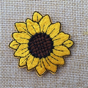 Peut inclure: Un patch brodé de tournesol jaune avec un centre brun. Le tournesol est sur un fond de tissu tissé.