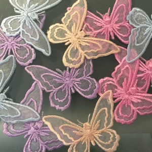 May include: Assortment of delicate butterfly appliques in shades of pink, purple, and blue. The appliques are made of sheer fabric with embroidered details.
