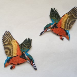 May include: Two embroidered iron-on patches of kingfishers in flight. The birds are orange, blue, green, and yellow with black outlines.
