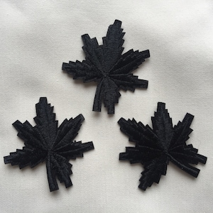 May include: Three black felt maple leaf patches. The leaves are stylised with jagged edges and a pointed tip.